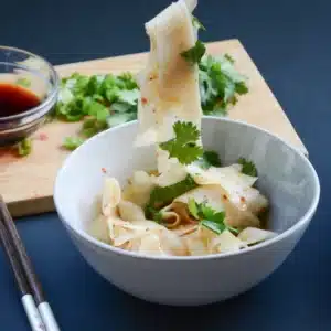Een schaal met koolrabi-noodle-salade staat op tafel met eetstokjes.